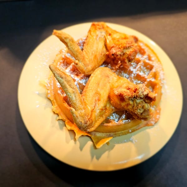 Golden-brown fried chicken wings and a waffle dusted with powdered sugar on a yellow plate.