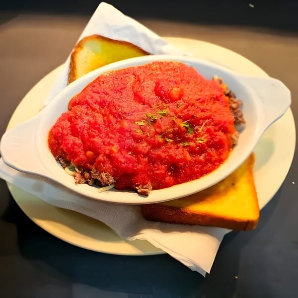 A white dish of spaghetti with meat sauce and two slices of buttered toast on a plate.