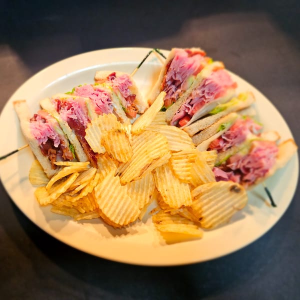 A diner-style club sandwich with deli meat, bacon, and lettuce, served with crinkle-cut chips.