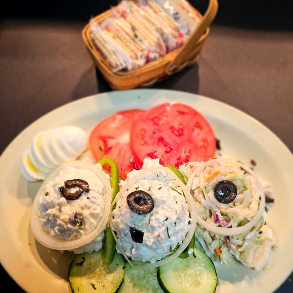 A diner plate with cottage cheese, coleslaw, sliced tomatoes, hard-boiled eggs, and cucumbers.