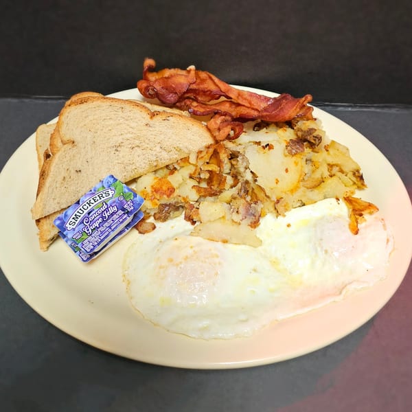 Diner breakfast plate with fried eggs, crispy bacon, hash browns, toast, and grape jelly.